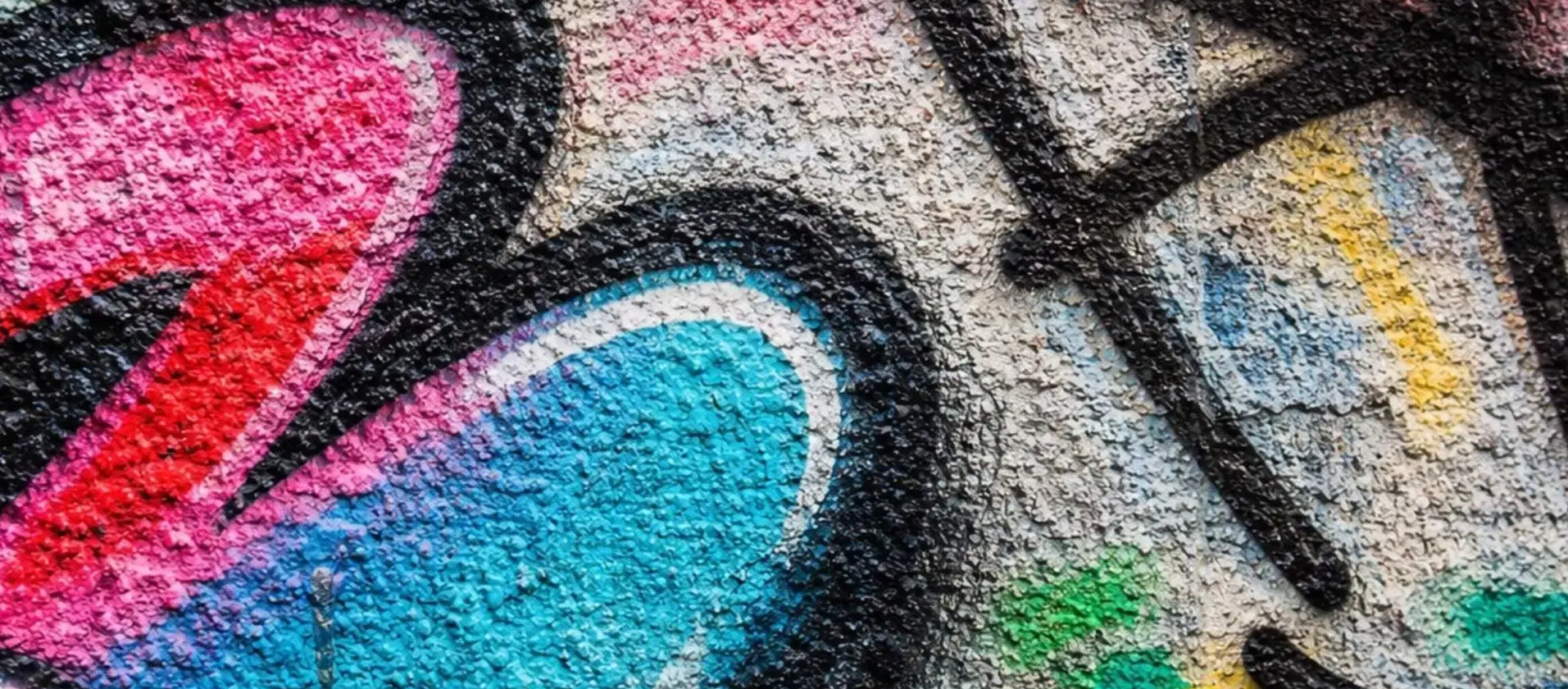 Close-up of colourful graffiti sprayed across textured walls, with thick paint outlines, layered colours, and visible rough concrete surface showing pits, cracks, and uneven texture beneath the artwork.